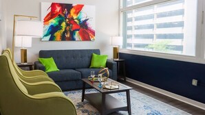 A modern living room with a sofa, green armchairs, a coffee table, and a colorful abstract painting. - EXECUTIVE STAY+KING BED+WIFI+W/D+PETS (Indianapolis)