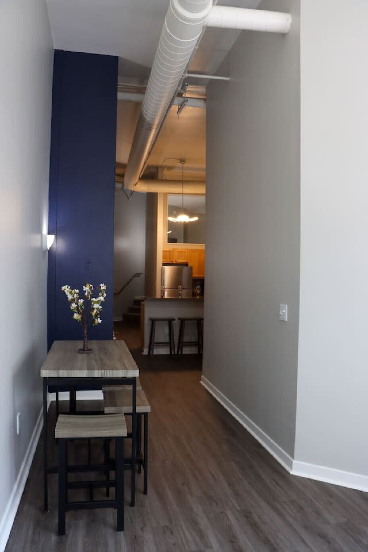 Un pasillo estrecho con una mesa y sillas de madera, una pared azul decorativa y una zona de cocina al fondo.