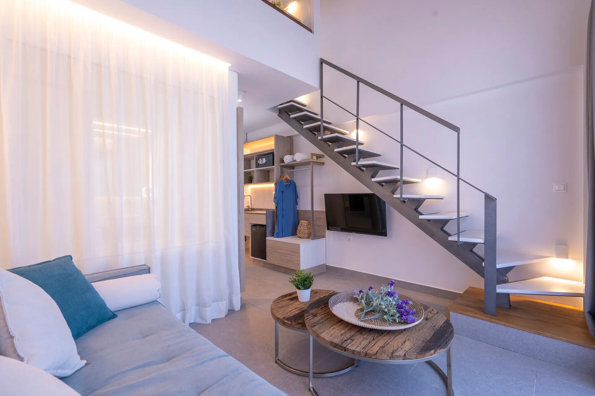 A modern living room with a staircase, a sofa, a coffee table, and a TV mounted on the wall.