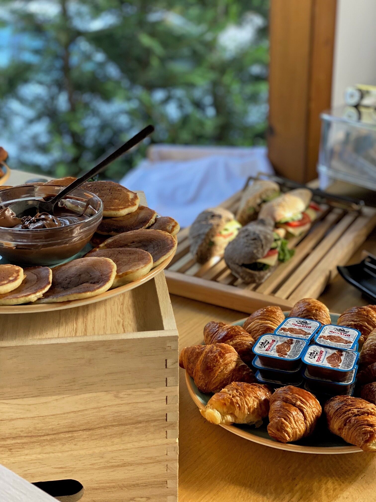A breakfast buffet with pancakes, croissants, sandwiches, and chocolate spread.