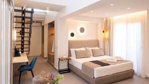 A modern hotel room with a large bed, a desk, and a dining area. - Mirablue Luxury Residences (Kassandra)