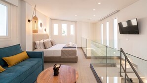 A modern bedroom with a bed, a sofa, a TV, and a glass railing. - Mirablue Luxury Residences (Kassandra)