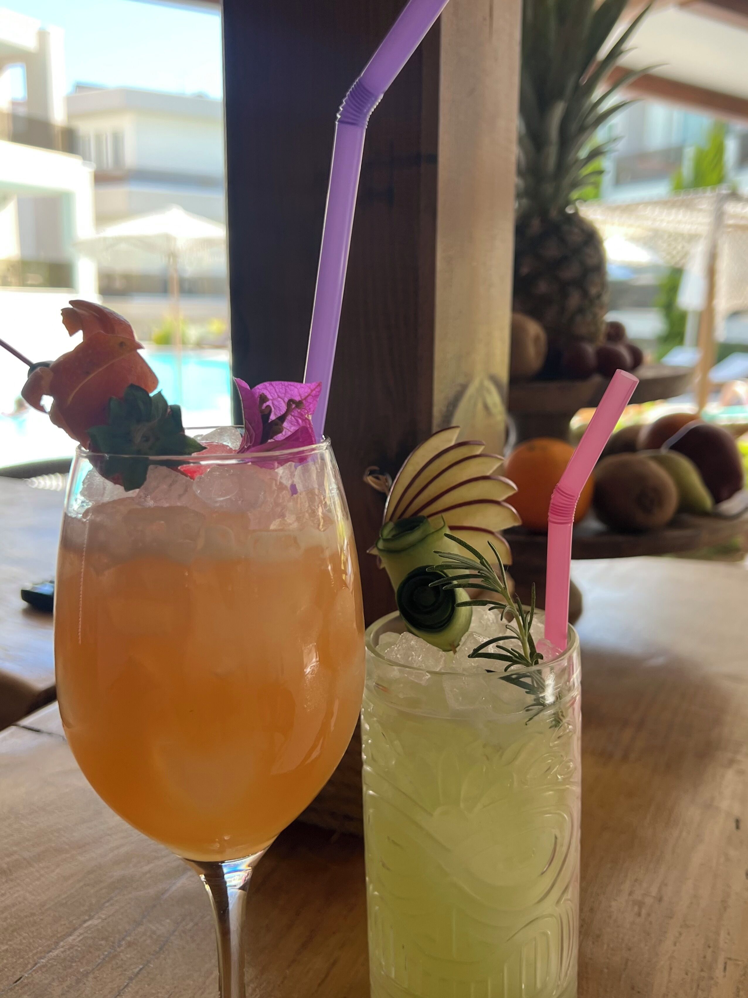 Twee drankjes met rietjes, een in een kelkglaas en een in een hoog glas, beide met decoratieve details.