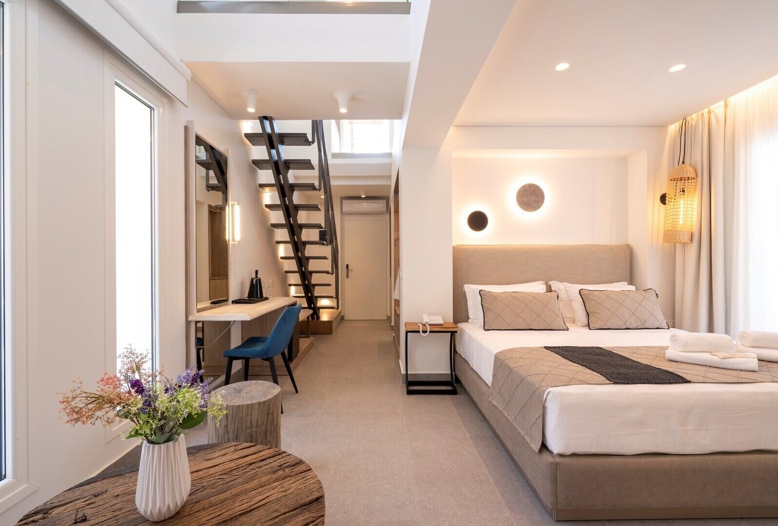 Una habitación de hotel moderna con cama, escritorio, silla y una escalera que conduce a otro nivel.