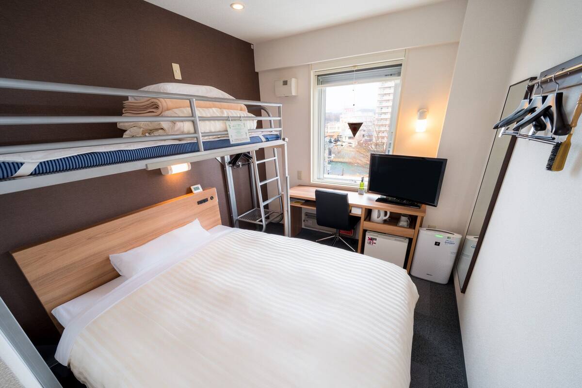 Una habitación de hotel con literas, un escritorio con computadora, una silla y un refrigerador pequeño.