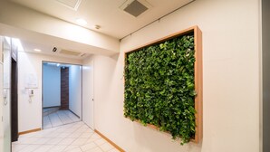 A hallway with a tiled floor, a wooden-framed wall-mounted plant, and a door leading to another room.