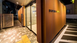 A hotel entrance with a modern design, featuring a wooden facade and a clear sign reading "SUPERHOTEL".
