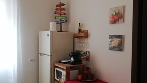 A compact kitchen with a refrigerator, microwave, and wooden table with chairs. There are wine glasses on a rack and a small shelf with a bottle. - The house with an Italian chef inside (Bologna)
