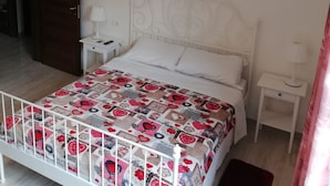 A bedroom with a white bed, a decorative quilt, a nightstand, a lamp, and a painting on the wall. - The house with an Italian chef inside (Bologna)