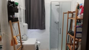 A compact bathroom with a bathtub, toilet, and shower. There is a wooden shelf with cleaning supplies and a green bucket. - The house with an Italian chef inside (Bologna)