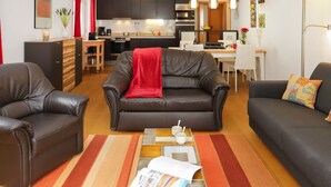 Een moderne woonkamer met een bruine leren bank, een salontafel met tijdschriften en een gestreept vloerkleed.