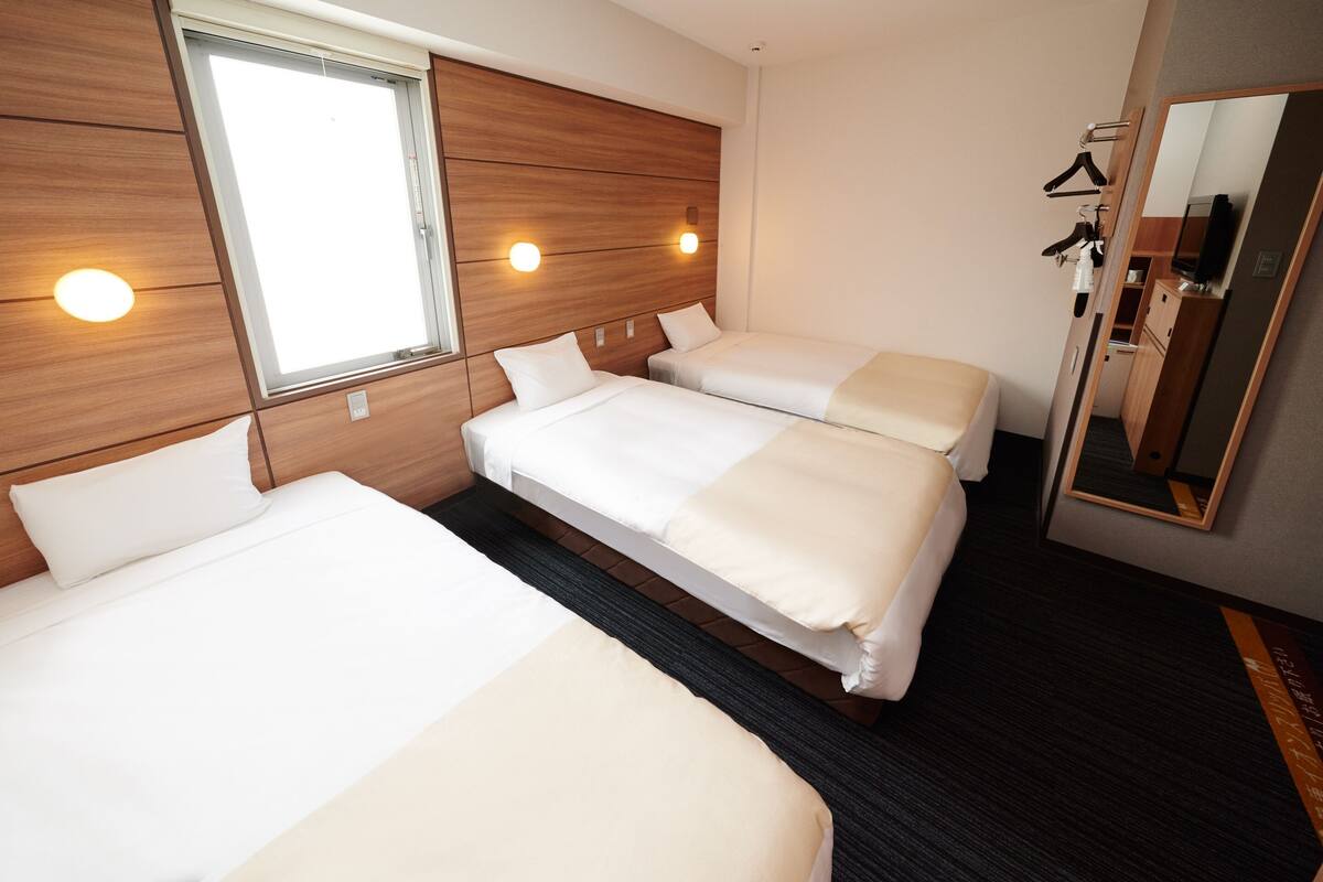 A hotel room with two beds, a large window, a mirror, and a wardrobe.