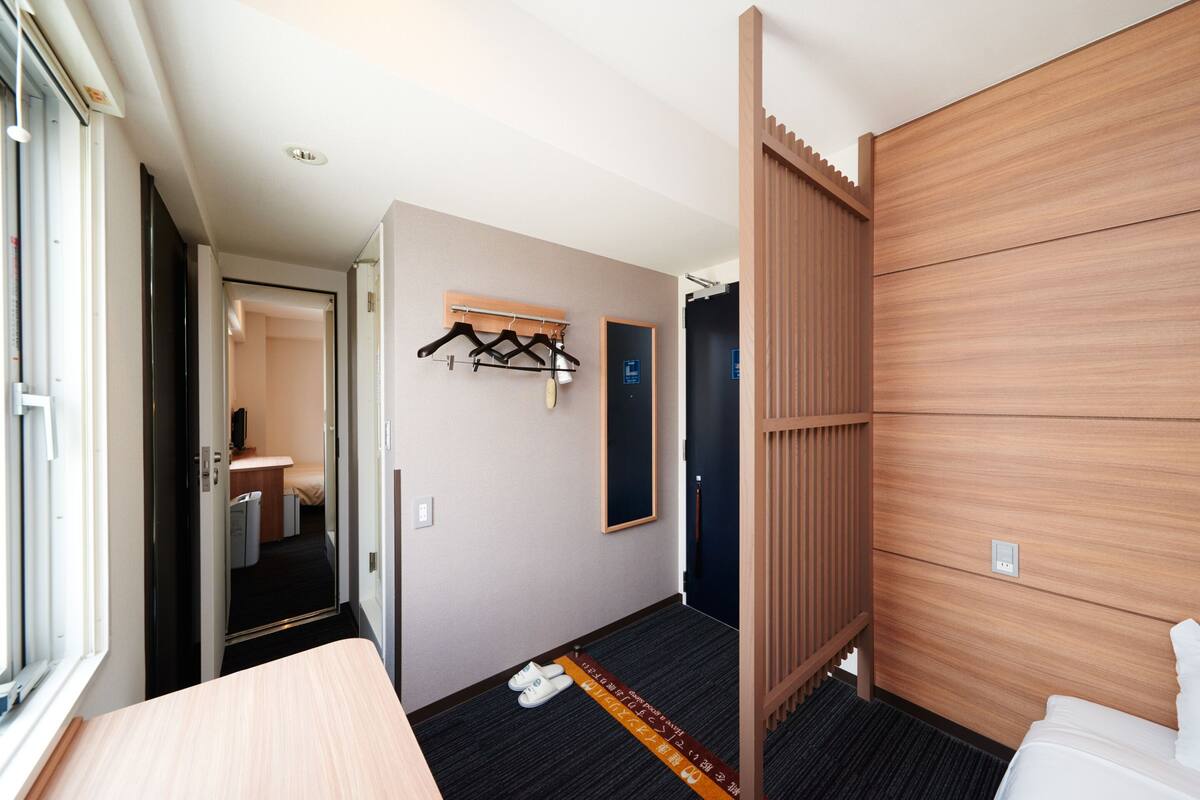 A hotel room with a bed, a wooden partition, a coat rack, and a door leading to a bathroom.