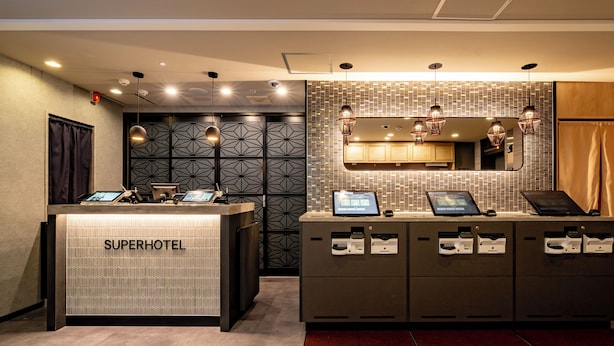En receptionsdisk märkt med texten ”SuperHotel”, utrustad med digitala incheckningskiosker, en vägg med ett intressant mönster och en modern belysningslösning.