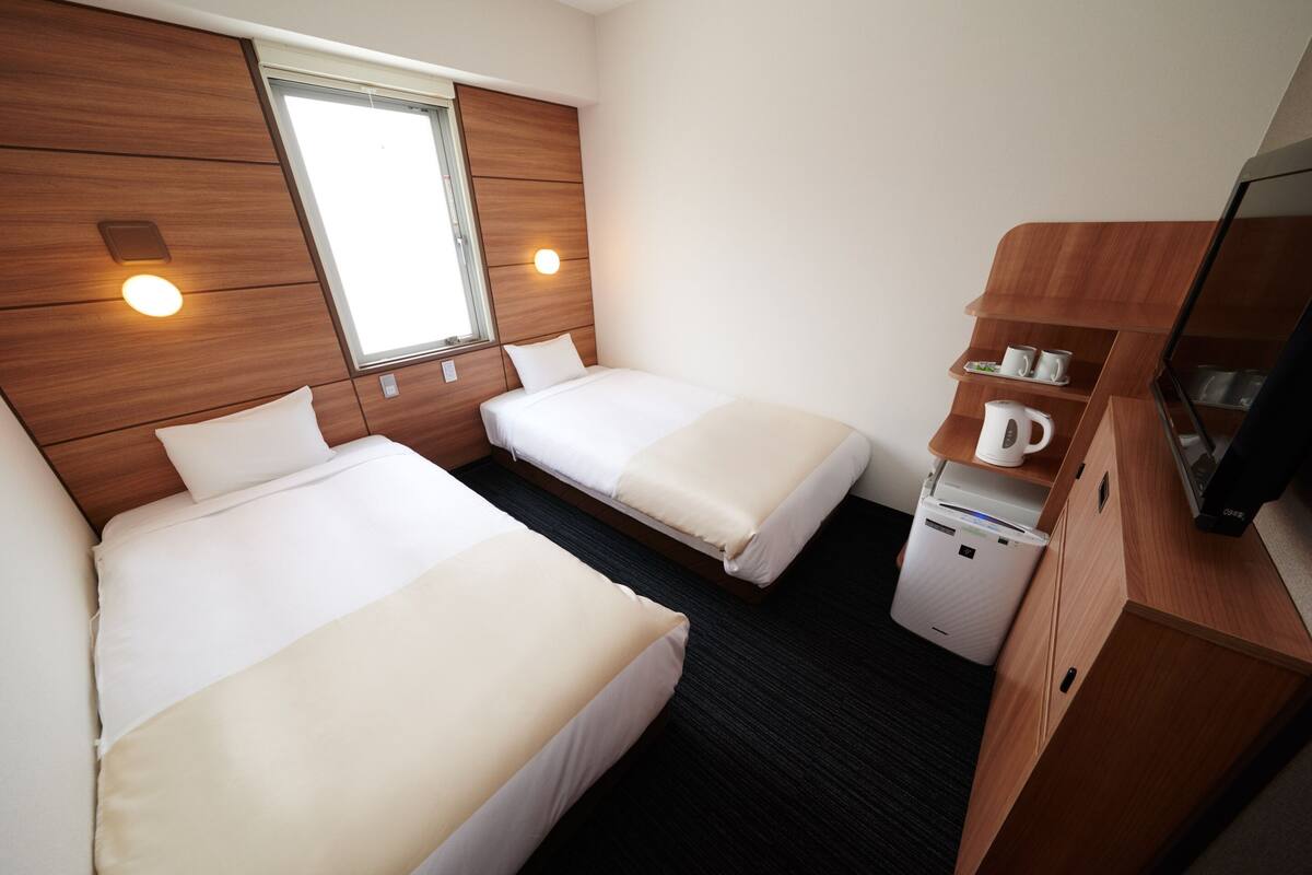 A hotel room with two beds, a window, a wooden cabinet with a coffee maker, and a television.