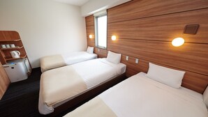 Ett hotellrum med två separata sängar, en sänggavel i trä, ett litet pentry och ett fönster.