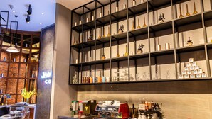 Een moderne barruimte met een koffieapparaat, planken met verschillende flessen en een bakstenen muur op de achtergrond.