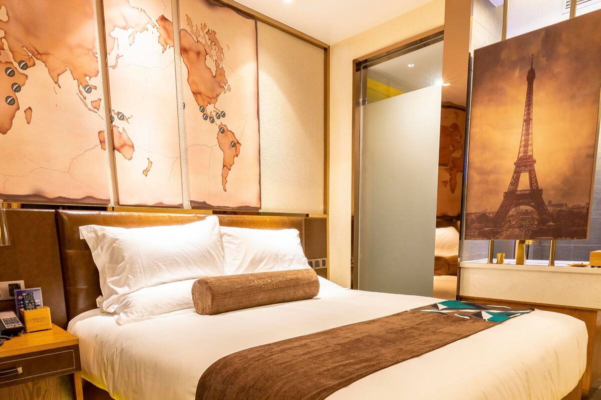 Une chambre d’hôtel avec un grand lit, une tête de lit en bois, une carte du monde accrochée au mur et une affiche de la Tour Eiffel.