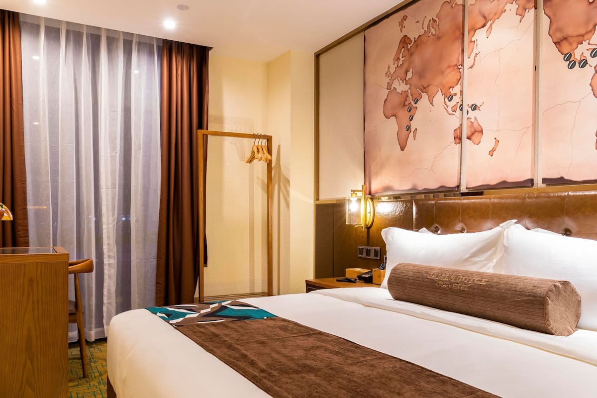 Une chambre d’hôtel avec un grand lit, un bureau, une chaise, une carte accrochée au mur et une table de chevet avec une lampe.