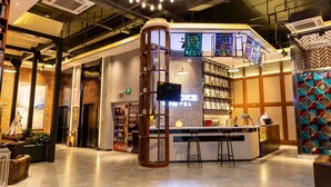 Een moderne hotelentree met een centraal gelegen bar, een groot verlicht bord en een opvallend plafondontwerp.