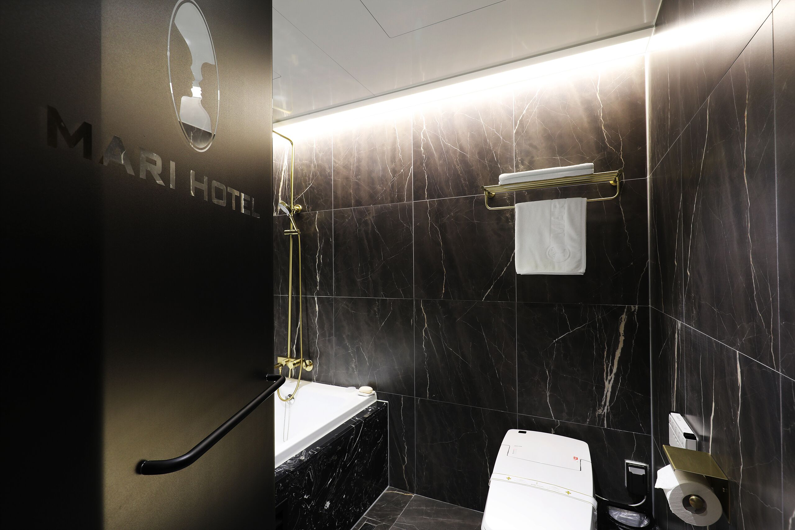 Un bagno moderno con una parete in marmo nero, un portasciugamani dorato, un water bianco e un box doccia in vetro.
