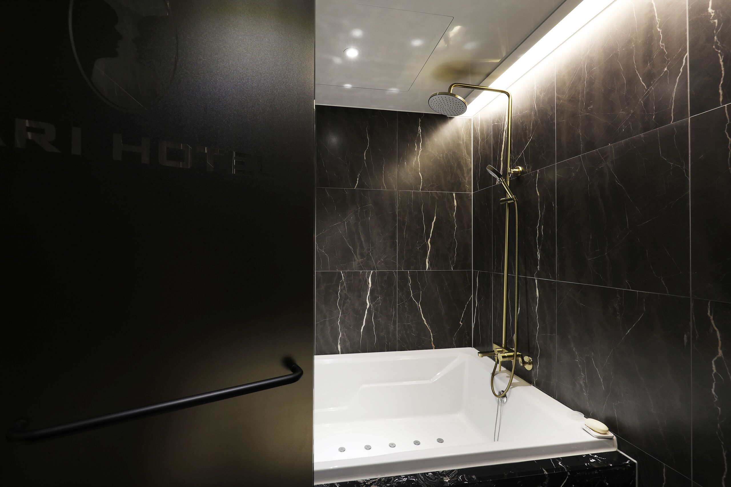 Une salle de bain moderne avec une baignoire blanche, une pomme de douche dorée et des carreaux de marbre noir.