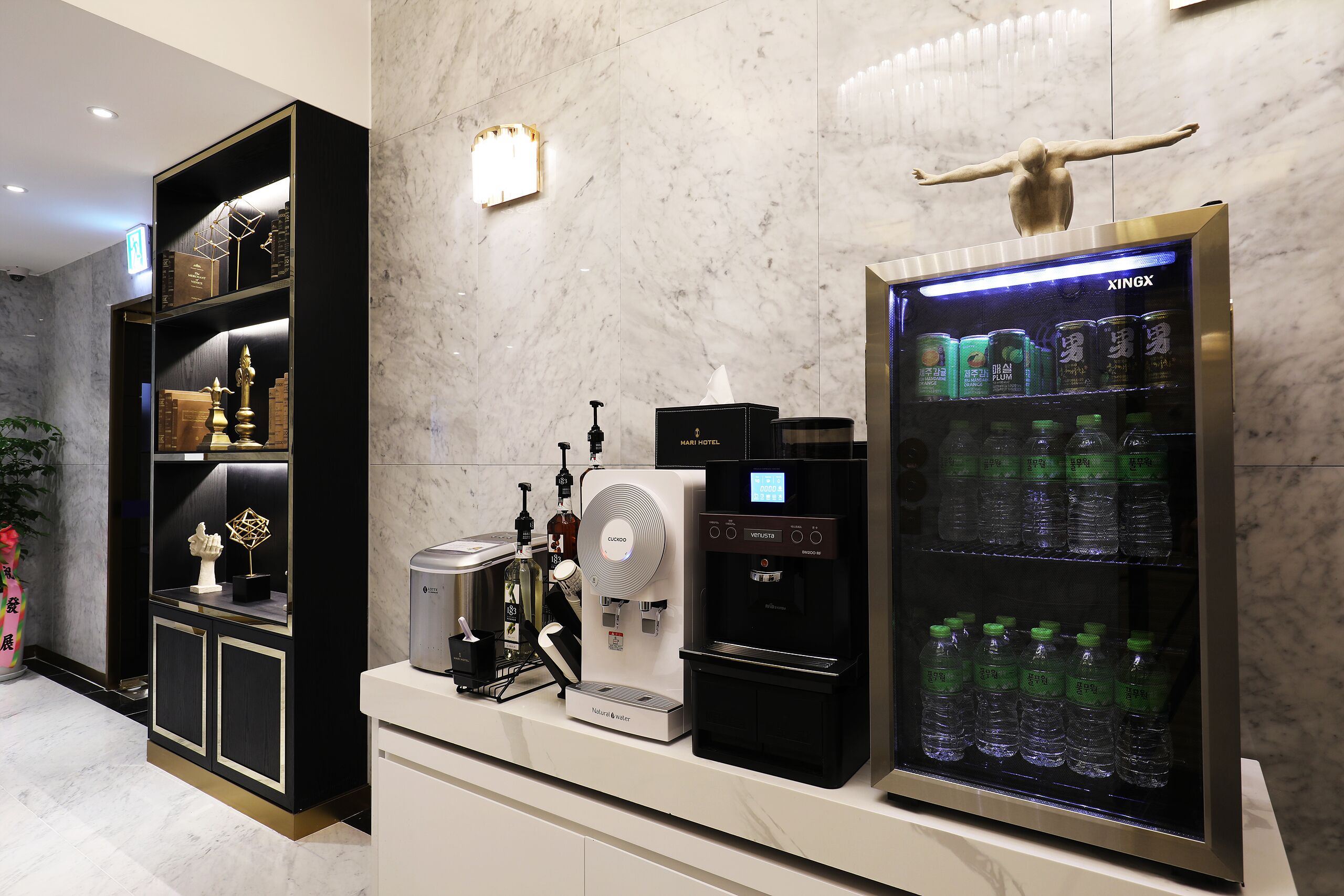 A hotel reception area with a water dispenser, a beverage refrigerator, and a display cabinet with decorative items.