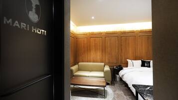 A hotel room with a wooden panel wall, a beige sofa, a bed with white bedding, and a marble coffee table.