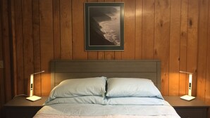Une chambre à coucher avec un mur lambrissé en bois, un lit avec une literie bleu clair, deux lampes de chevet et un tableau représentant un paysage.
