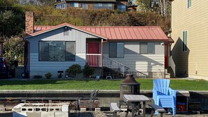 Une maison avec un toit rouge, un porche à l’avant et une petite terrasse.