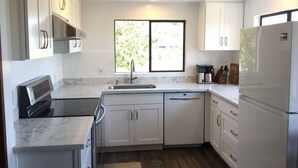 Une cuisine moderne avec des meubles blancs, un four encastré, un lave-vaisselle et un réfrigérateur.