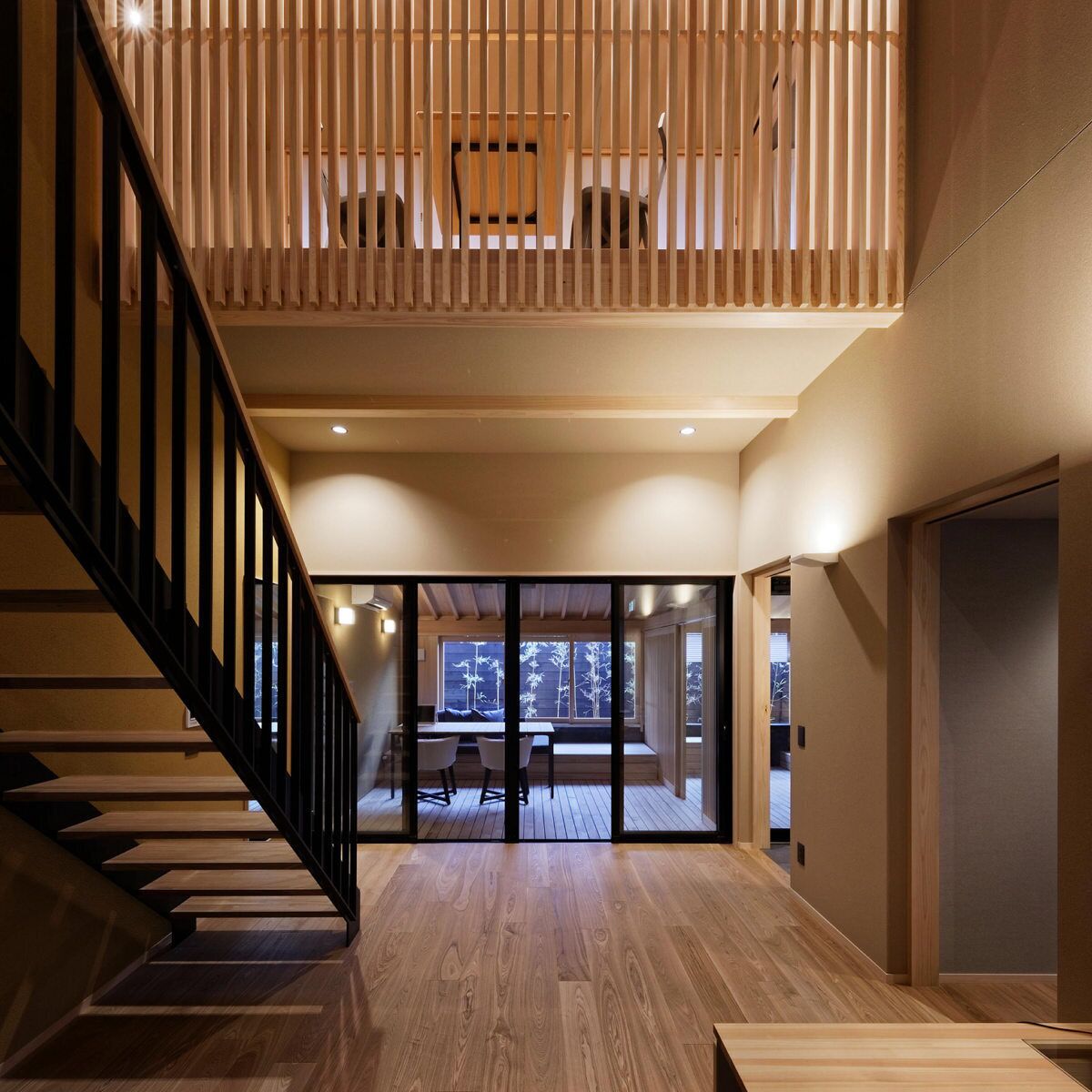 Un intérieur moderne avec un escalier en bois, un coin repas et une vue à travers des portes vitrées.