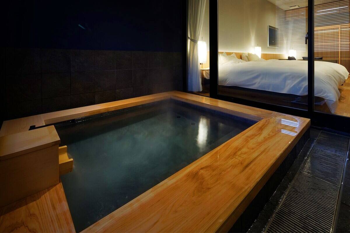 Ein modernes Hotelzimmer mit einer großen Glaswand, einer Holzbadewanne und einem ordentlich bezogenen Bett.