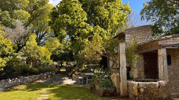 Un edificio de piedra con fachada rústica, rodeado de un jardín cuidado con un sendero de piedra que lleva a un banco de madera.