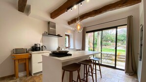 Cocina moderna con una isla central, taburetes de bar y un amplio ventanal corredero que da a un espacio exterior.