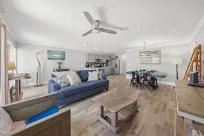 A modern living room with a blue sofa, a wooden coffee table, and a dining area with a table and chairs. - Best location in SK Village, Walk to Beach (Sarasota)