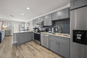 A modern kitchen with grey cabinets, stainless steel appliances, and a stone backsplash. - Best location in SK Village, Walk to Beach (Sarasota)