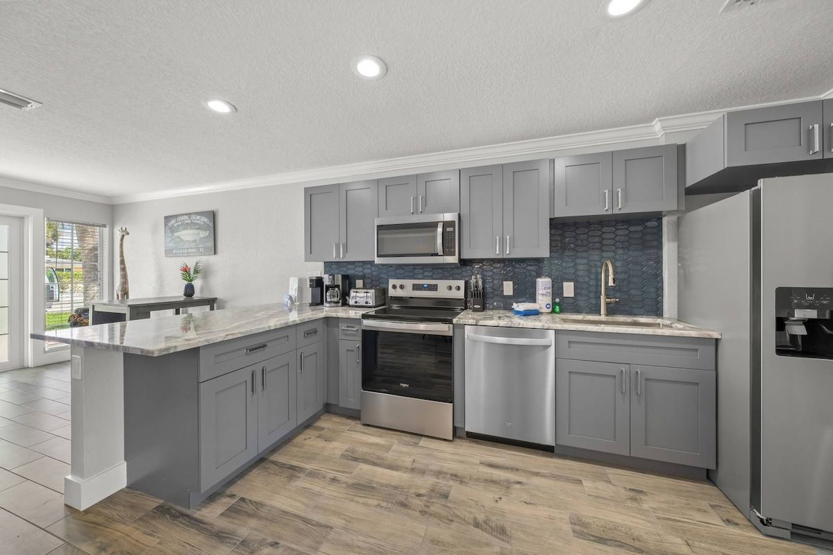 A modern kitchen with grey cabinets, stainless steel appliances, and a large island.