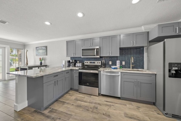 A modern kitchen with grey cabinets, stainless steel appliances, and a large island.