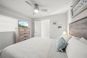 A bedroom with a bed, a ceiling fan, a TV, a dresser, and a wall-mounted sign.