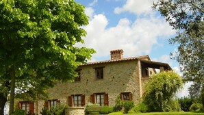 A stone house with a tiled roof, surrounded by a well-maintained lawn and trees.