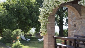 An outdoor seating area with a wooden bench and a stone archway covered in white flowers.