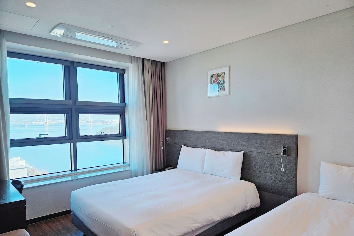 A hotel room with a large window, a bed, a bedside table, and a wall-mounted TV.