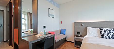 A modern hotel room with a bed, a desk, a chair, a nightstand, and a large mirror.