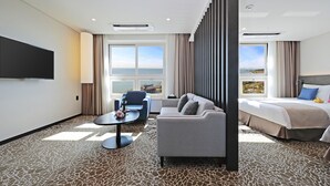 Habitación de hotel con cama, sofá, televisión, ventana grande con vistas y alfombra estampada.