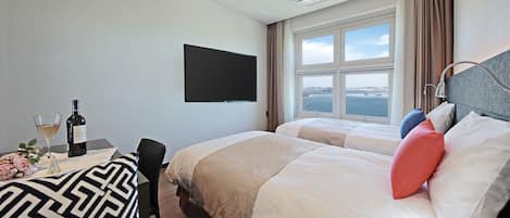 A hotel room with two beds, a TV, a window with a view, and a table with a bottle and glass.