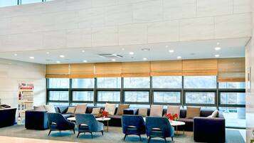 Um hall amplo com design moderno, apresentando uma área de estar com sofás e poltronas, janelas grandes e um chão de azulejos impecável.