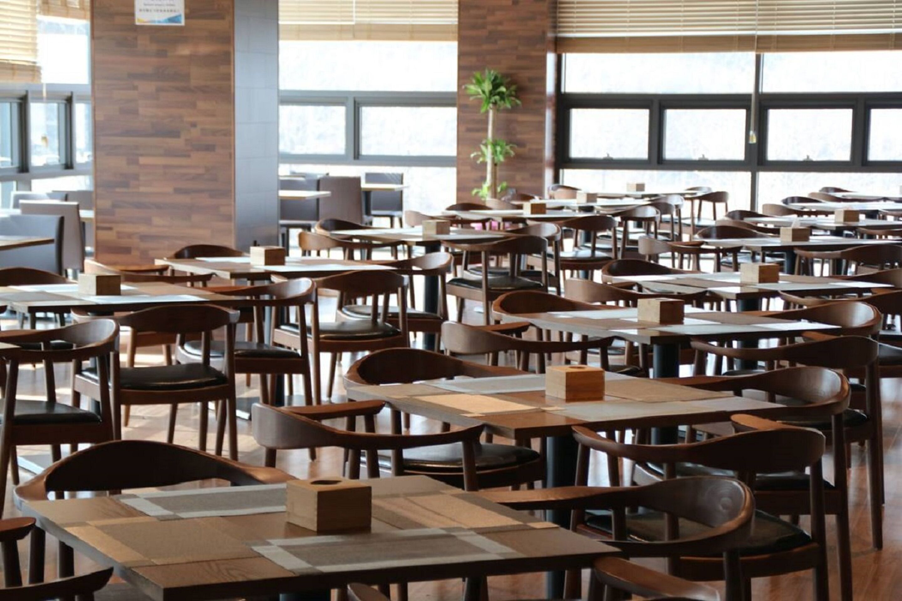 A spacious restaurant with multiple tables and chairs, large windows, and a brick wall.