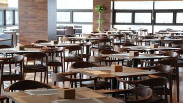 A spacious restaurant with multiple tables and chairs, large windows, and a brick wall.