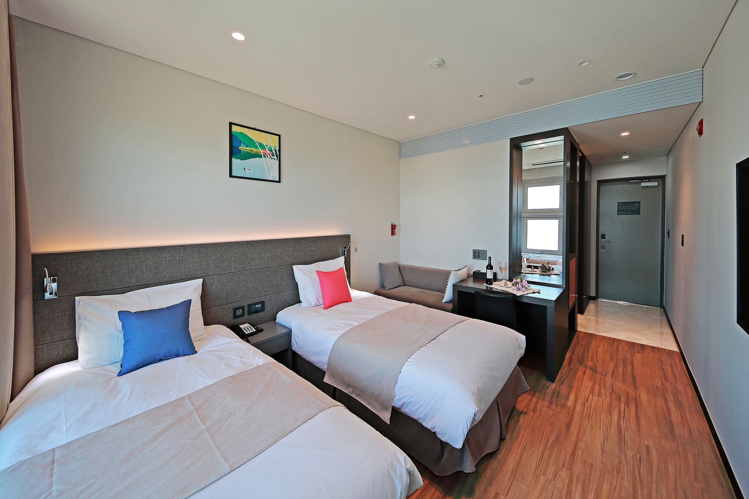 A hotel room with two beds, a desk, a chair, and a mirror.